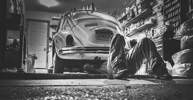 A mechanic working underneath a car, photographed from the ground.